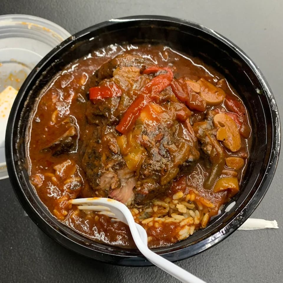 Hearty American stew with meat, red peppers, and mushrooms over rice, served in a black bowl.