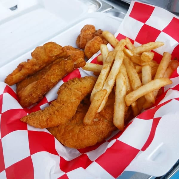 Crispy fried chicken tenders, popcorn chicken, and golden french fries in a red and white checkered basket.