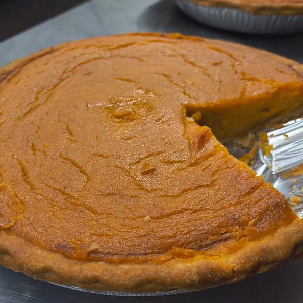 A partially eaten pumpkin pie in a foil tin, with a slice removed, on a dark surface.