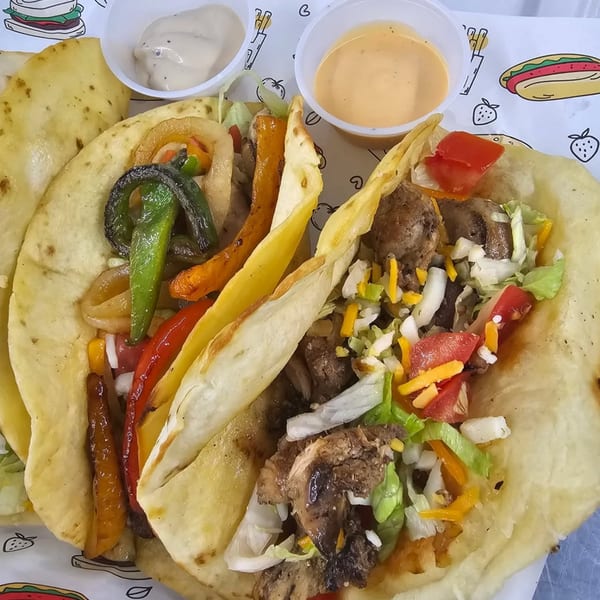 Two American-style tacos with meat, cheese, lettuce, and peppers, served with two dipping sauces.