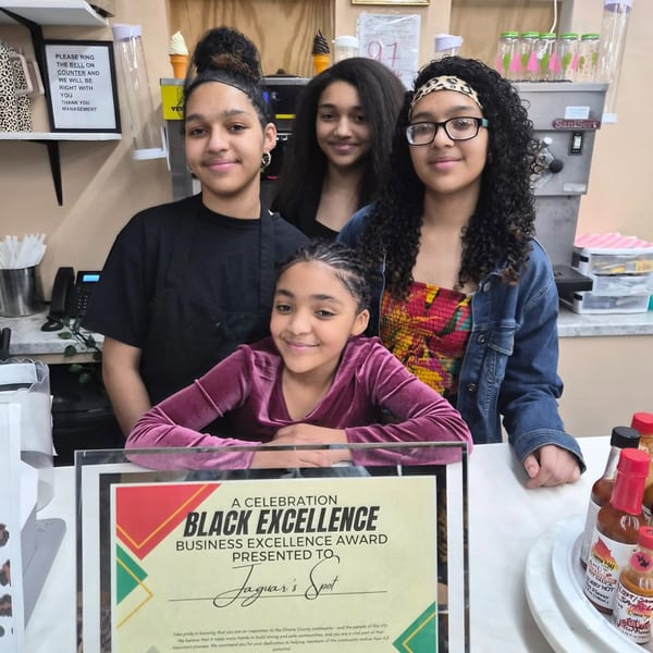 Four young women smiling behind a counter, with a "Black Excellence" award for Jaguar's Spot.