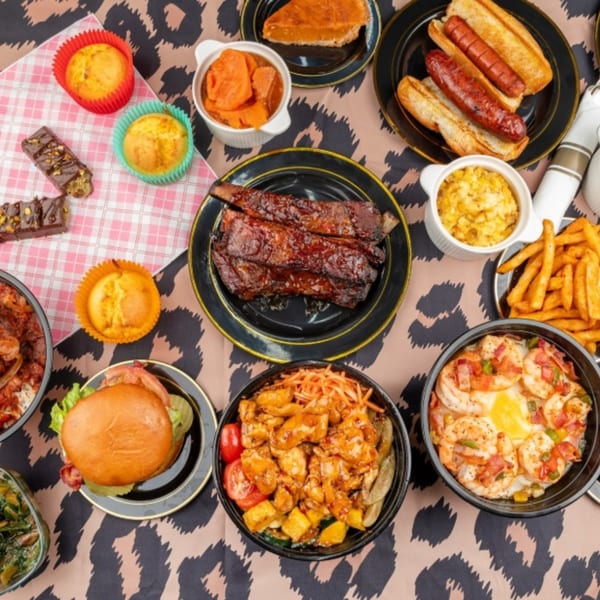 An overhead view of a feast of Southern comfort food, including ribs, hot dogs, shrimp and grits, and muffins.