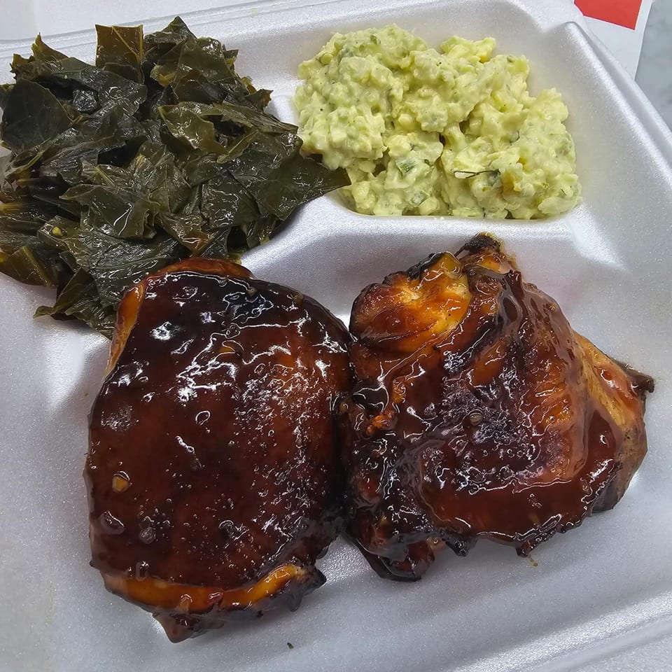 BBQ chicken with collard greens and potato salad in a white takeout container from Jaguar's Spot.