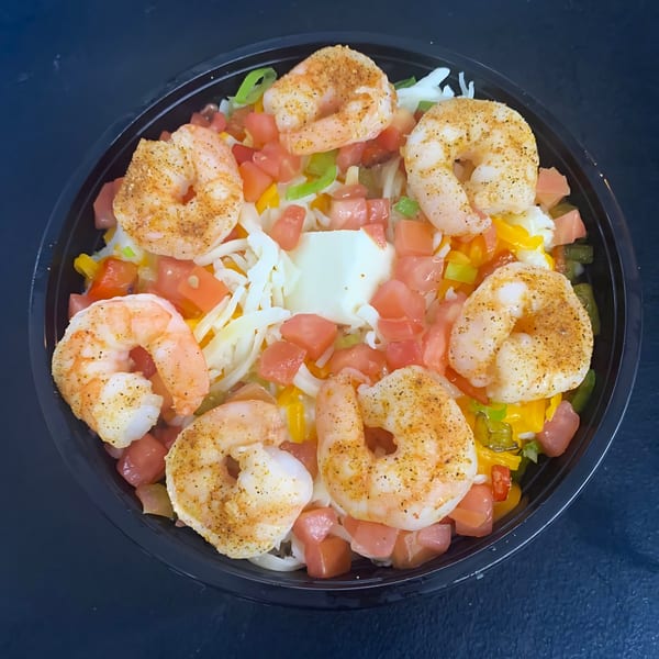 A black bowl filled with seasoned shrimp, diced tomatoes, bell peppers, shredded cheese, and a dollop of sour cream.