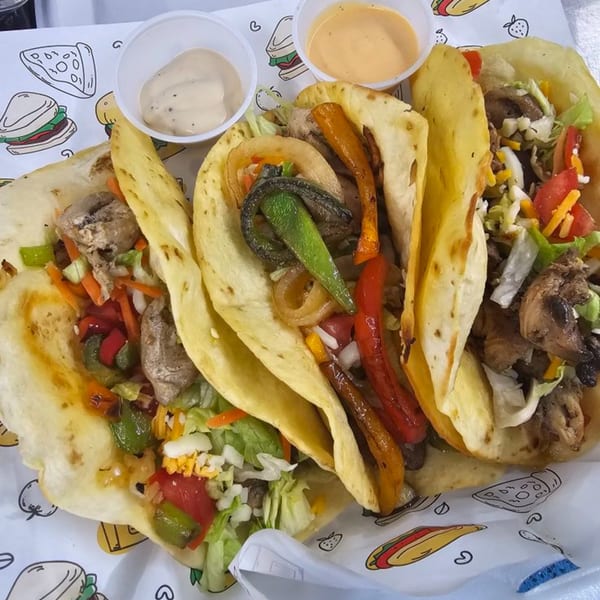 Three American-style tacos with various fillings, including grilled vegetables, meat, and cheese, with dipping sauces.