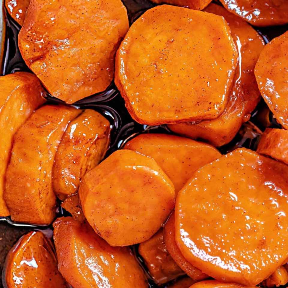 Close-up of candied sweet potatoes glistening in a dark, sweet syrup, sprinkled with spices.