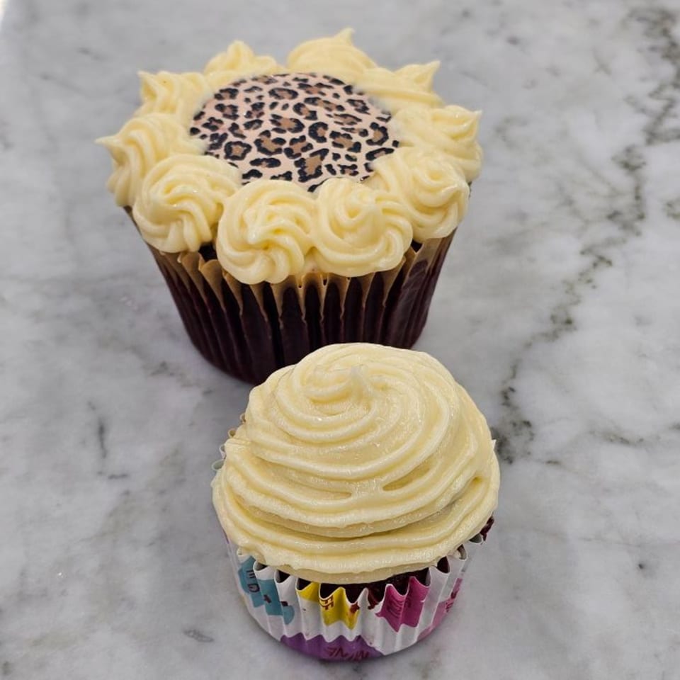 Two cupcakes on a marble surface, one large with leopard print, one small with swirled frosting.