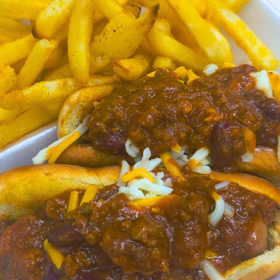 Two chili cheese dogs with shredded cheese and a side of golden french fries.