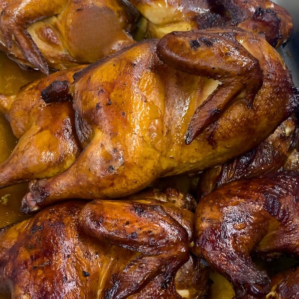 Close-up of several whole roasted chickens with glistening, golden-brown skin in a pan.