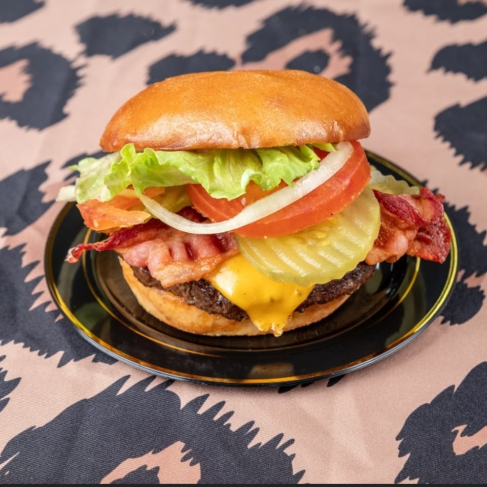 A bacon cheeseburger with lettuce, tomato, onion, and pickles on a black plate.