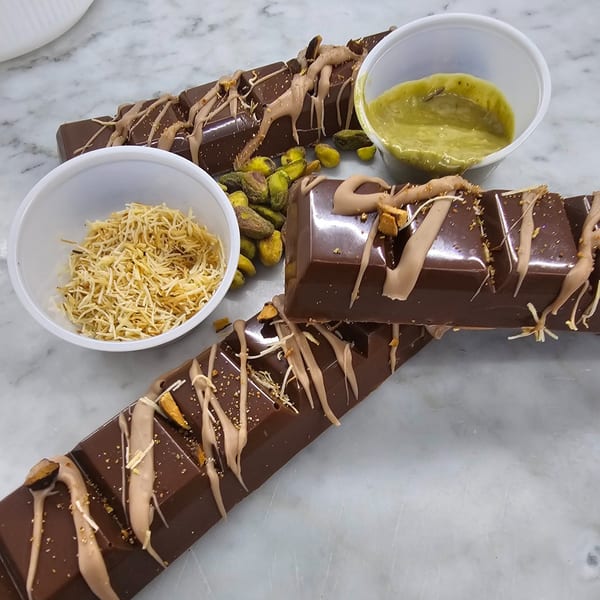 Three chocolate bars drizzled with caramel, pistachios, and shredded coconut on a marble surface.